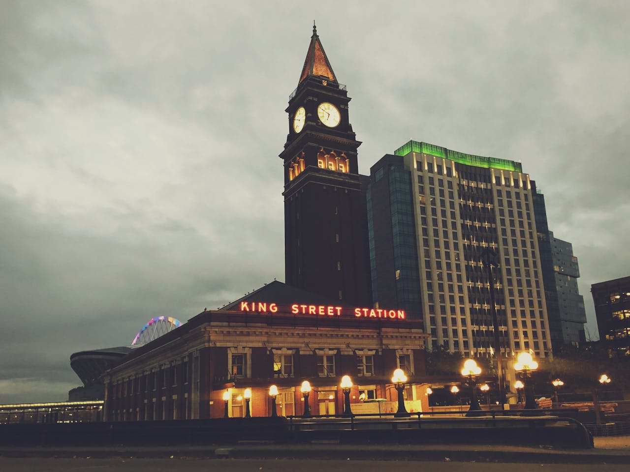 A view of King Street Station against a Seattle cityscape at dusk.